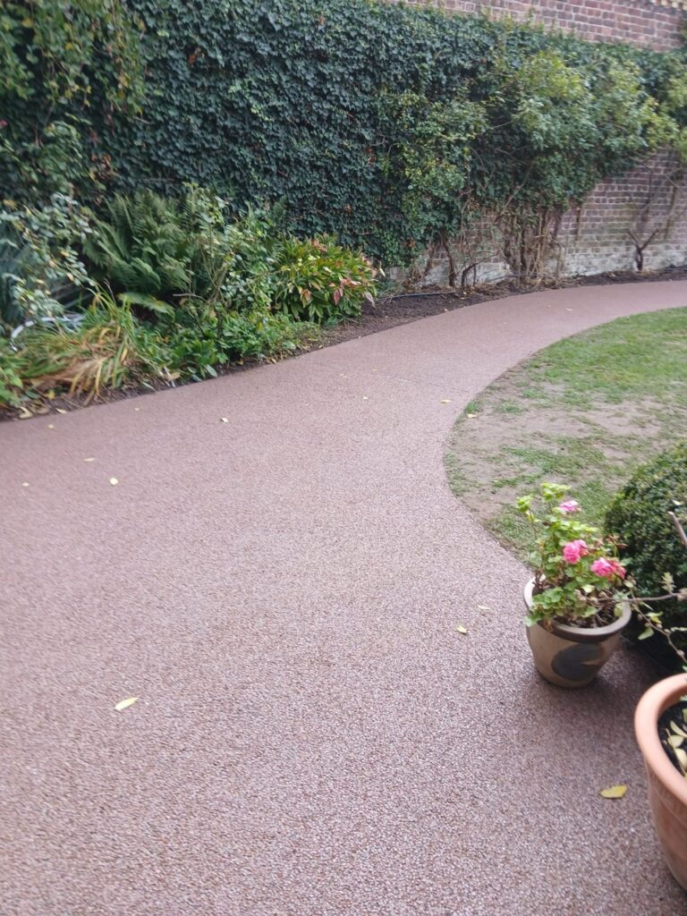Sierlijk gebogen tuinpad met fijn Terradec steentapijt naast groene planten en blote aarde